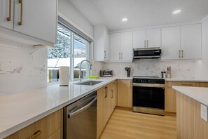 A modern kitchen with white cabinets, a stainless steel microwave, a dishwasher, and a large window.