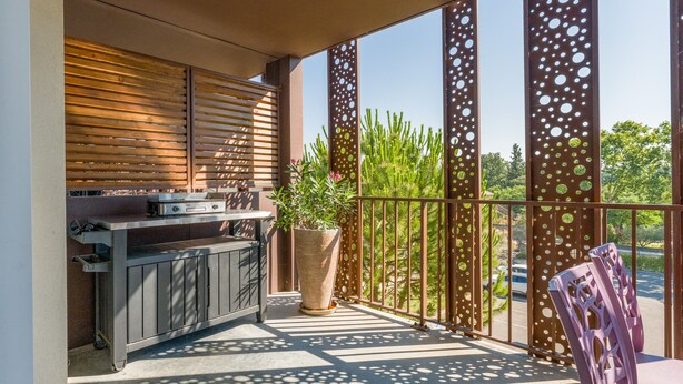 An outdoor balcony with a grill, potted plants, and a chair.