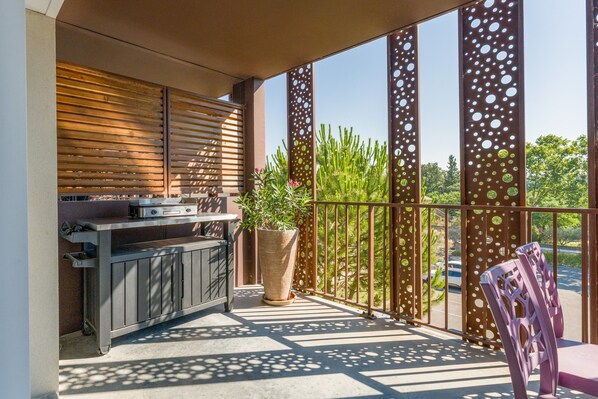 An outdoor balcony with a grill, potted plants, and a chair.