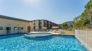 A swimming pool with a circular hot tub, lounge chairs, and umbrellas.