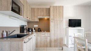 A modern kitchen with wooden cabinets, a built-in microwave, a coffee maker, and a television on a stand.