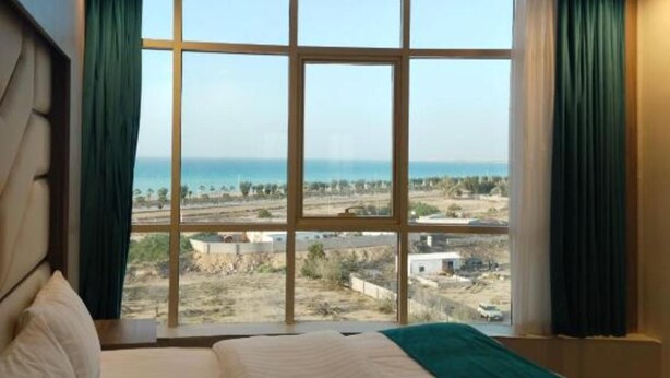 A bedroom with a large window, a bed, and curtains. - HMM Serviced apartments Umluj (umm lajj)