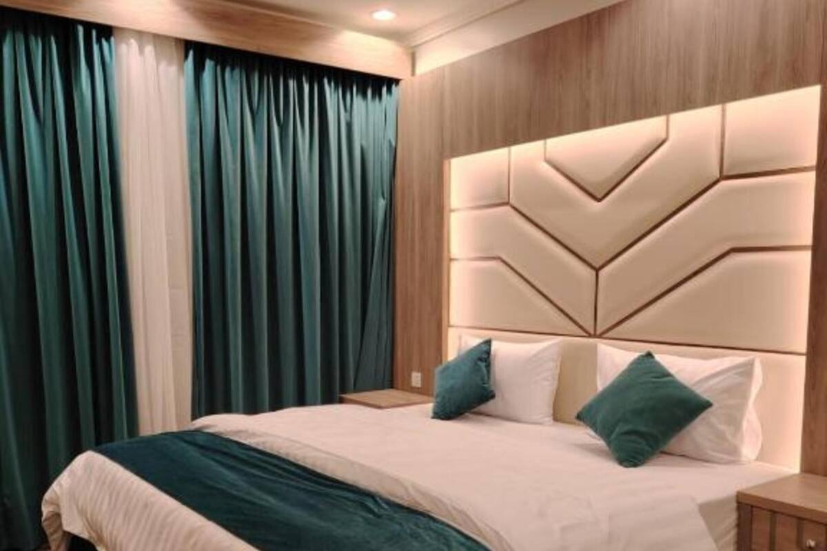 Una cama bien hecha con cabecera, mesita de noche y alfombra estampada.