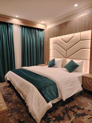 A neatly made bed with a headboard, a bedside table, and a patterned carpet. - HMM Serviced apartments Umluj (umm lajj)