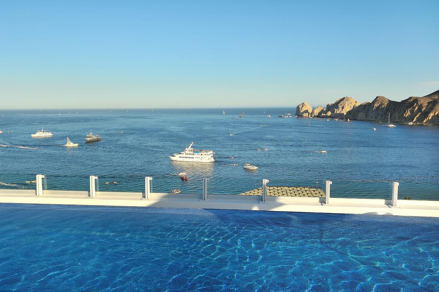 A clear blue pool with a view of the sea and boats.