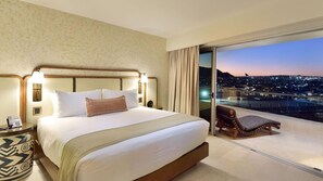Camera d'albergo con un letto grande, un comodino, una sedia e un balcone con vista sulla città.