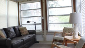 Ein Wohnzimmer mit einer Ledersofa, zwei Sessel, einer Lampe und Blick durch große Fenster.