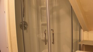 Eine Eckdusche mit Glastür, Toilette und Duschkopf.