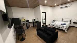 Une chambre d’hôtel moderne équipée d’un lit, d’un bureau avec une chaise, d’un canapé, d’un miroir et d’un appareil de climatisation.