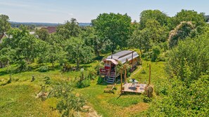 A house surrounded by lush greenery, with a small porch and outdoor seating area. - Circus Wagon in Ostrach – Unique Caravan in the Orchard (Ostrach)