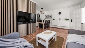 Ein modernes Wohnzimmer mit Fernseher, Esstisch, Stühlen und einer Couch.