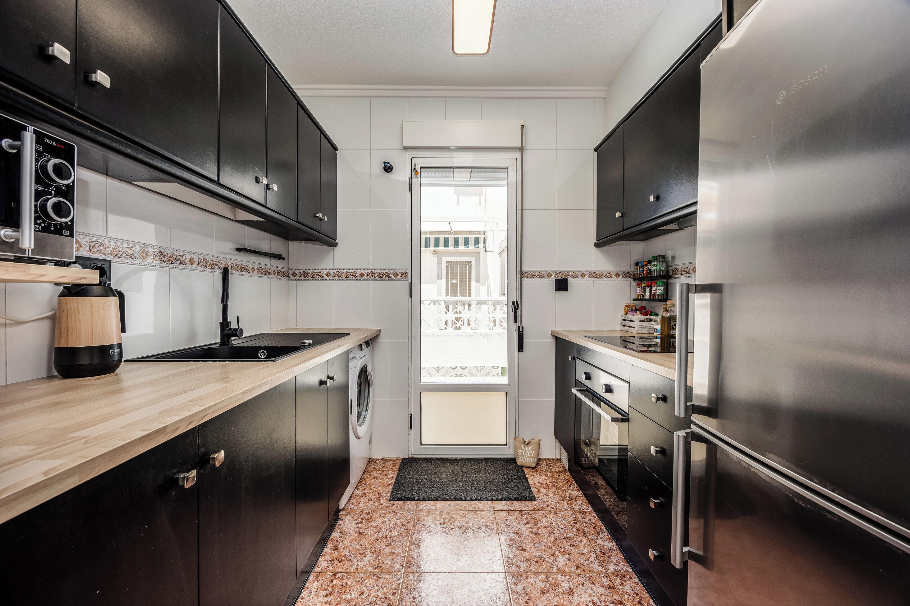 A compact kitchen with a washing machine, a built-in oven, and a stainless steel refrigerator.