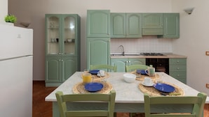 A kitchen with green cabinets, a white refrigerator, and a dining table set with blue plates and yellow cups. - Casa del Leccio F4 by Wonderful Italy (San Teodoro)