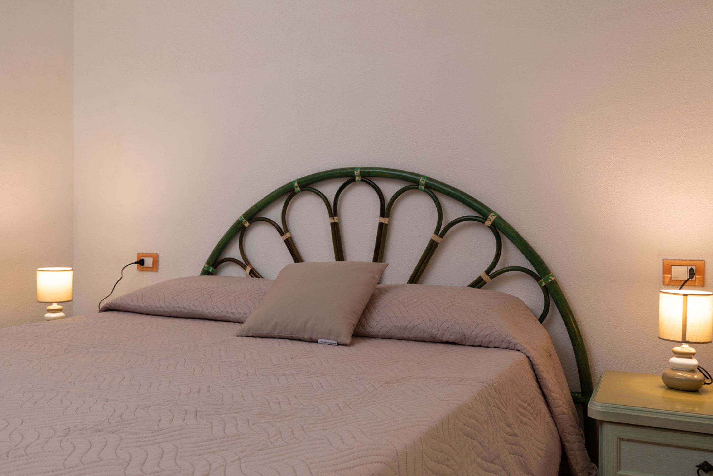 A bed with a headboard, two bedside lamps, and a bedside table.