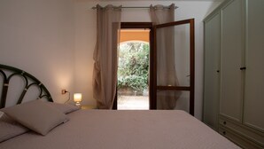 A bedroom with a bed, a nightstand with a lamp, a wardrobe, and a door leading to an outdoor area. - Casa del Leccio F4 by Wonderful Italy (San Teodoro)
