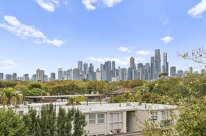 Städtische Skyline mit Hochhäusern, blauem Himmel und Grünpflanzen im Vordergrund.