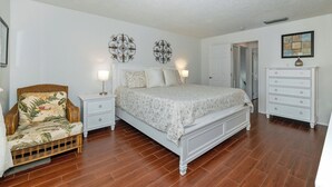 Un dormitorio con cama, mesitas de noche, cómoda, silla y decoración en la pared.