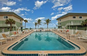 Ein Swimmingpool mit Liegestühlen und Palmen, umgeben von Gebäuden mit Balkonen.
