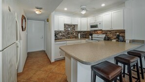 Una cocina con armarios blancos, encimera de granito, microondas y ventilador de techo.