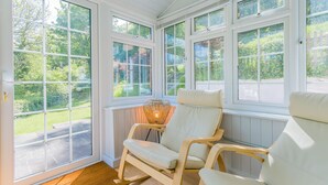 A sunroom with large windows, a wicker chair, and a view of the garden. - Dulas Bach - sleeps 12 guests  in 6 bedrooms (Colwyn Bay)