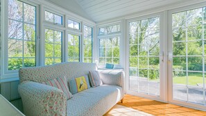 A conservatory with a floral-patterned sofa, multiple windows, and a view of greenery. - Dulas Bach - sleeps 12 guests  in 6 bedrooms (Colwyn Bay)