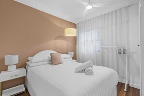 Ein Hotelzimmer mit Bett, Nachttisch, Lampe, Deckenventilator und einem Fenster mit Vorhängen.