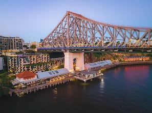 Eine Brücke mit Fachwerkkonstruktion, ein Restaurant am Wasser mit Außenbereich und ein Gebäude mit der Beschilderung 'Crystalbrook VINCENT'.