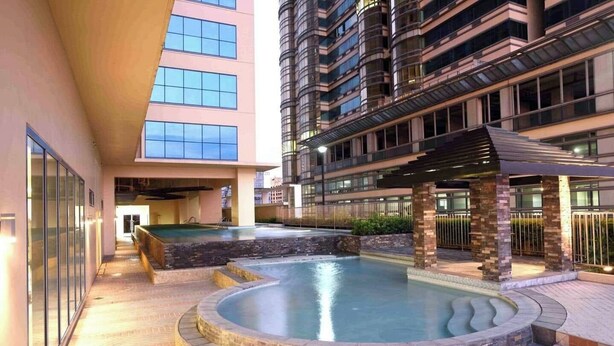 A swimming pool area with a curved design, surrounded by a building with multiple floors and large windows. - Grand Riviera Suites Manila Bay Stay (Manila)