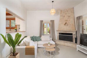 A modern living room with a sofa, a fireplace, a television, and a dining area. - Newly renovated 3 bedroom traditional cretan villa (Iraklio)