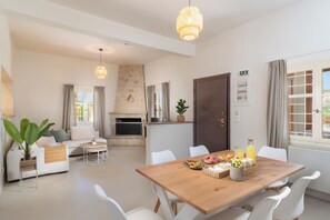 A modern living room with a fireplace, dining table, and white furniture. - Newly renovated 3 bedroom traditional cretan villa (Iraklio)