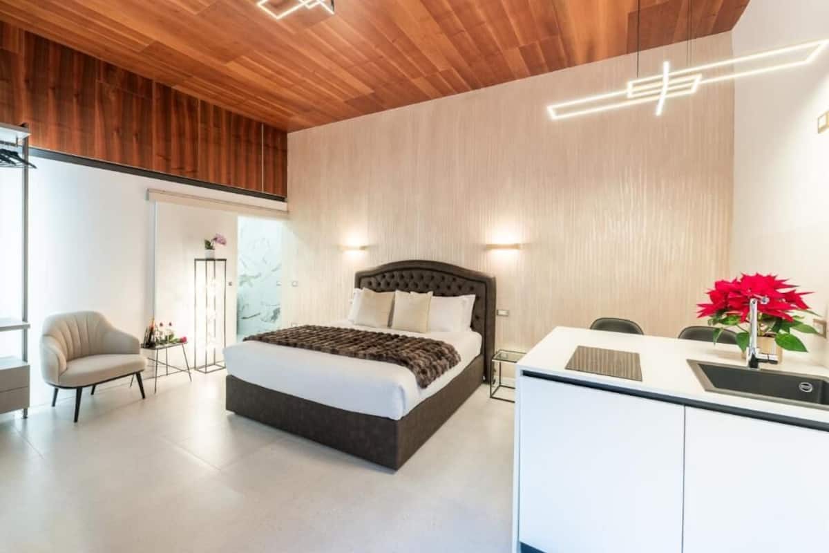 A modern bedroom with a large bed, bedside tables, a desk, and a chair.