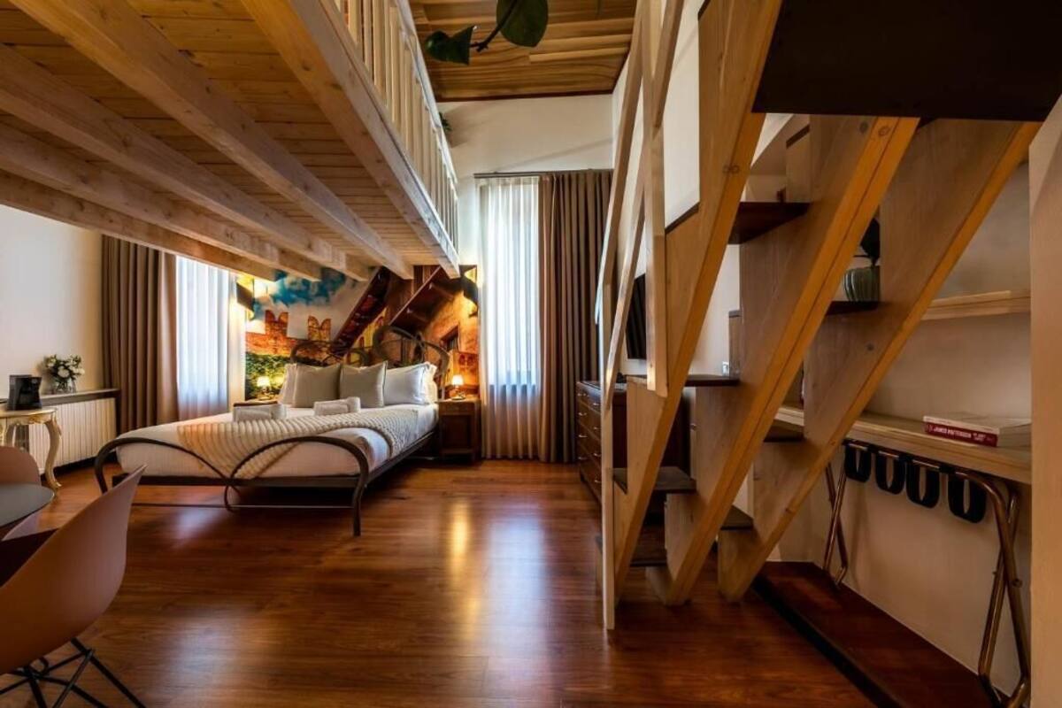 A bedroom with a bed, a desk, and a chair. There is a window with curtains and a view of the outside.