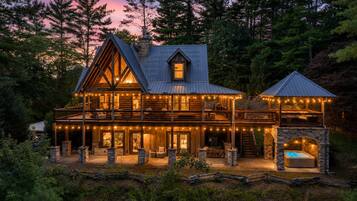 A log cabin with a stone fireplace, a covered porch, and a hot tub.