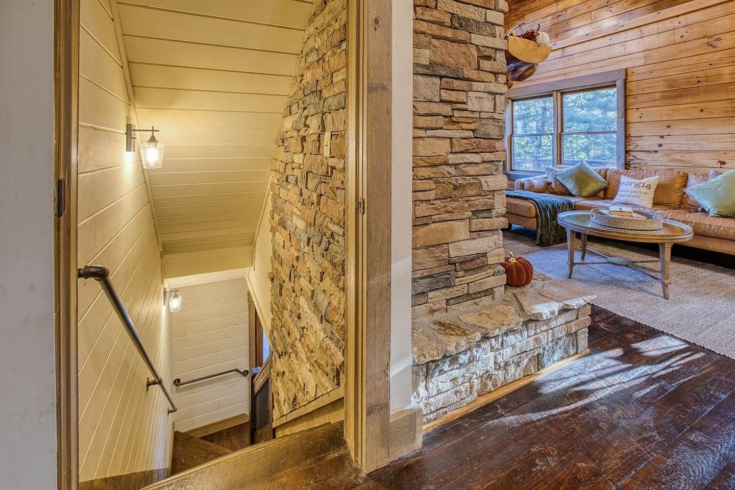 A wooden interior with a stone fireplace, a sofa with cushions, and a staircase.