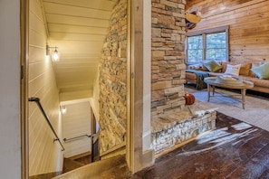 Un intérieur en bois avec une cheminée en pierre, un canapé avec des coussins et un escalier.