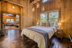 A wooden cabin interior with a large bed, a dining area, and a view of the outdoors. - Luxury Lodge: Mini Golf, Hot Tub, Views, Game Room, Pet Friendly (Gilmer County)