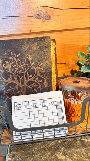 A wooden wall with a tree carving, a metal rack holding pens, and a scorecard labeled 'HOLES' with columns for players and holes. - Luxury Lodge: Mini Golf, Hot Tub, Views, Game Room, Pet Friendly (Gilmer County)