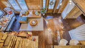 Ein Interieur einer Holzhütte mit Holzboden, Ledersofa, Esstisch gedeckt mit Geschirr und einem großen Fenster.