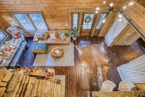 L’intérieur d’une cabane est doté d’un plancher en bois, d’un canapé en cuir, d’une table à manger avec de la vaisselle et d’une grande fenêtre.