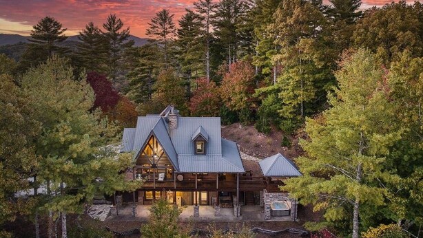 Eine Holzhütte mit großer Veranda und Whirlpool, umgeben von dichtem Wald.