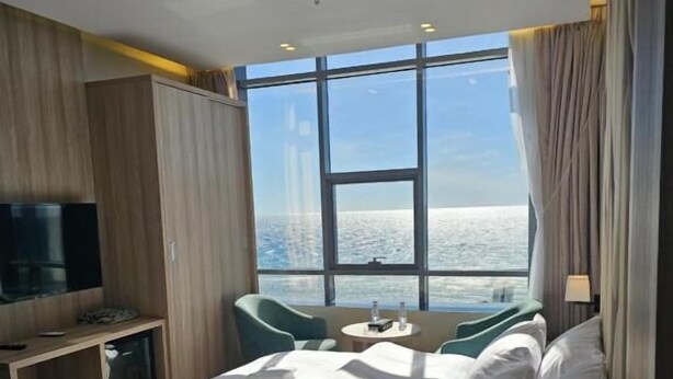 A hotel room with a large window, a bed, a desk, a chair, and a television.