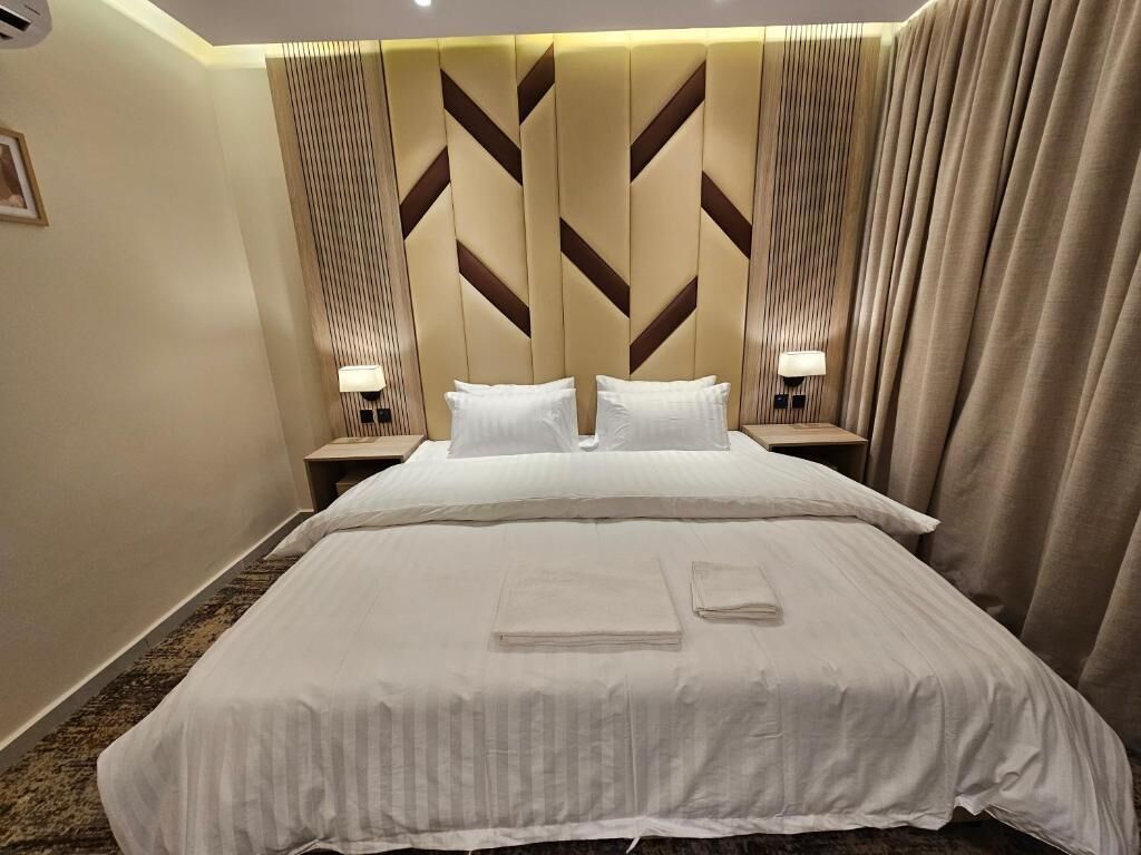 A hotel room with a large bed, two bedside tables with lamps, a headboard with a geometric pattern, and a curtain on the right side.