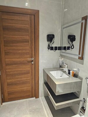 A bathroom with a wooden door, a vanity with a mirror, and a hairdryer on the wall. - Sea Gull hotel - فندق سي قل (Umluj)