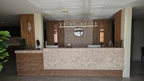 A reception area with a marble counter, wooden paneling, a round mirror, and a hanging light fixture.