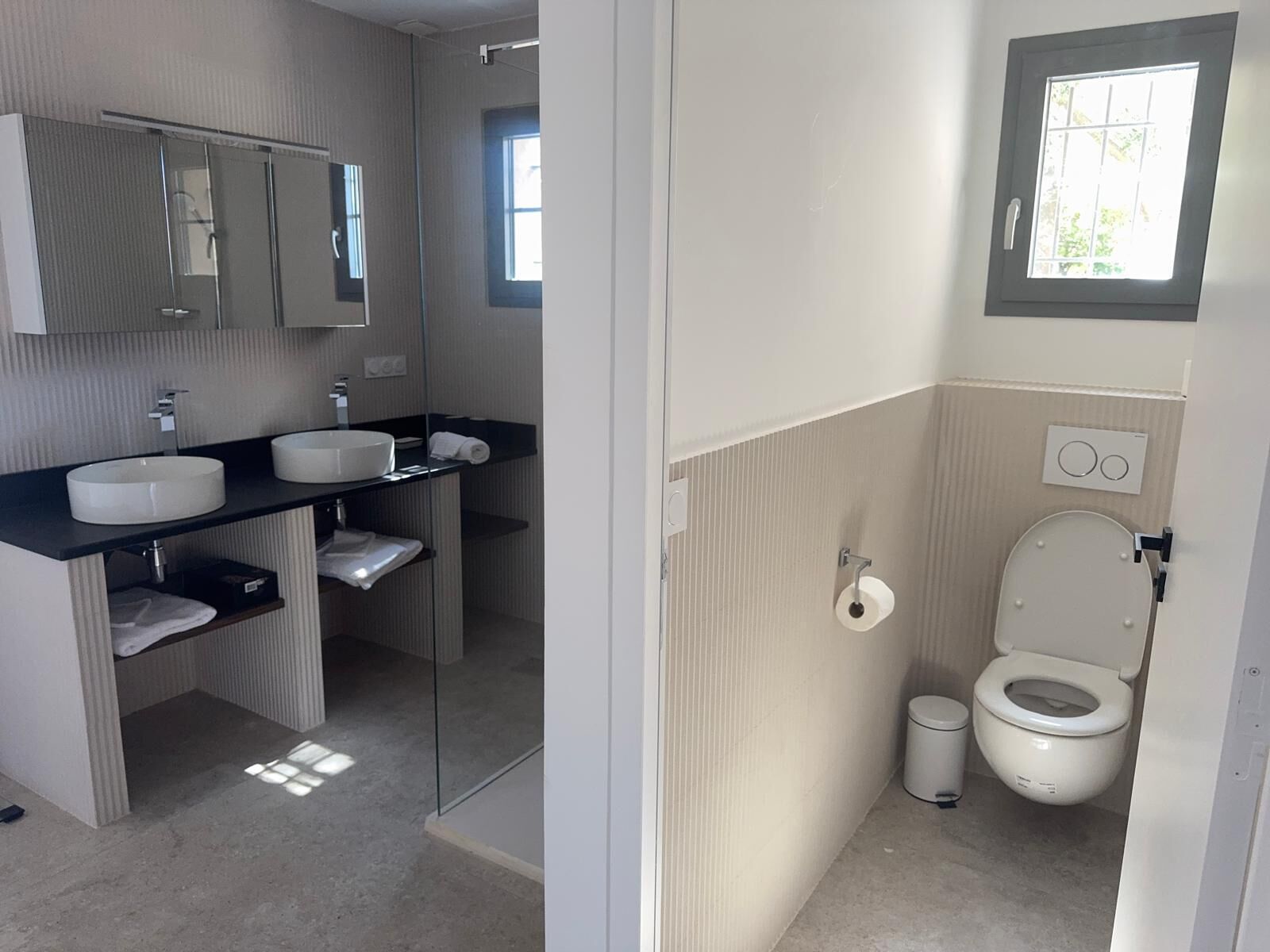 Ein modernes Badezimmer mit großem Spiegel, zwei Waschbecken, Toilette und Duschbereich.