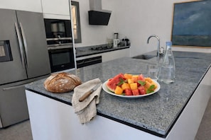 Eine moderne Küche mit einer Granit Arbeitsplatte, einem Brotlaib, einer Obstschale und einer Wasserflasche.