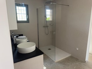 Ein modernes Badezimmer mit einer Duschkabine aus Glas, einem runden Waschbecken und einem Fenster für natürliches Licht.