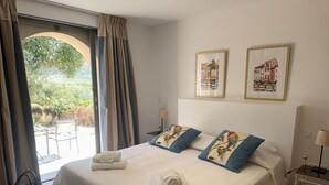 Een hotelkamer met een bed, twee kussens, een nachtkastje, een lamp en uitzicht op groen.