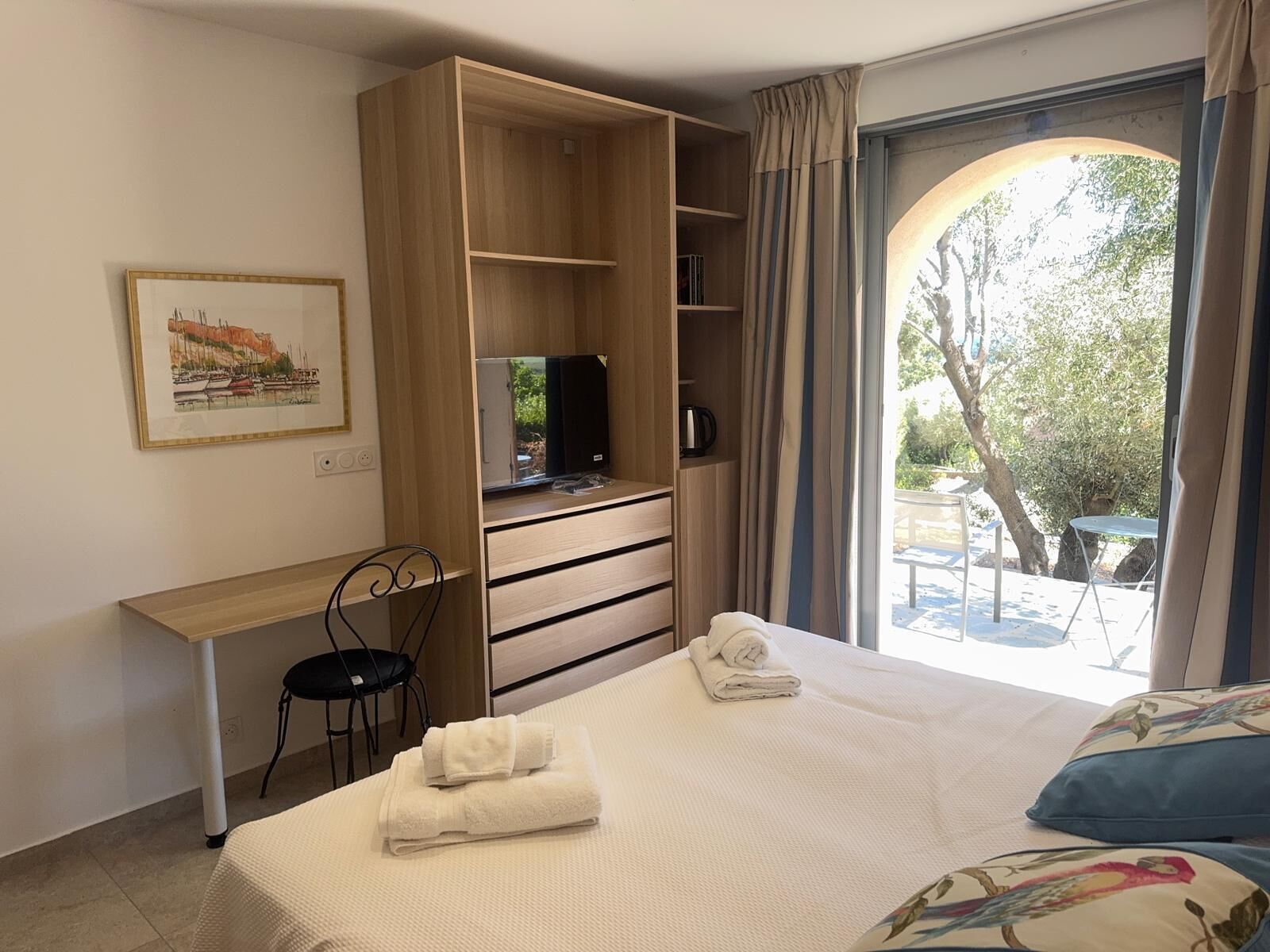 A hotel room with a bed, a desk, a chair, a TV, and a view of the outdoors.