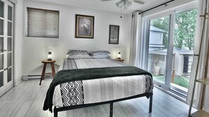 A bedroom with a bed, two bedside tables with lamps, a ceiling fan, and a large window with a view of the outdoors. - River & Nature - Nook Richelieu (Henryville)